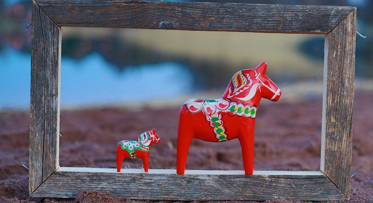 En liten och en stor röd dalahäst står i en ram