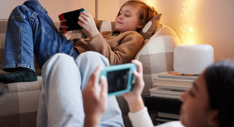 Två barn som halvligger i varsin soffa med mobil framför sig