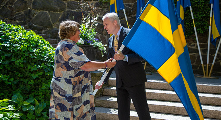 En kvinna tar emot en svensk fana ur handen på landshövding Sten Tolgfors.