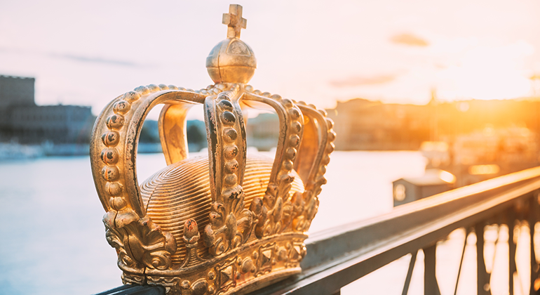 Krona i guld på broräcke, vatten och Stockholm syns i bakgrunden.