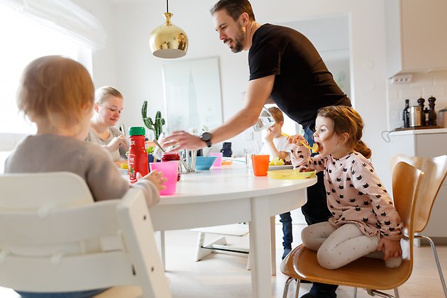 En familj med två små barn sitter runt ett köksbord och äter. 